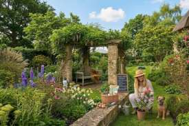 Home gardener planting flowers in a beautiful landscaped backyard garden with pergola, lawn, and blooming plants during regular garden maintenance.