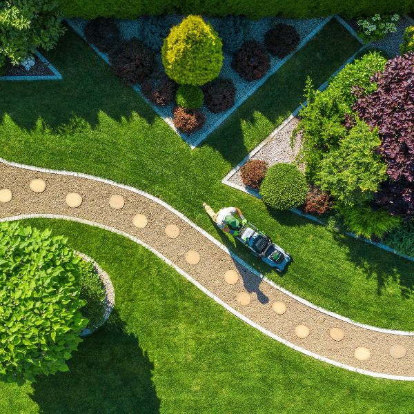 Aerial view of professional lawn mowing service with gardener using lawn mower on green landscaped garden pathway