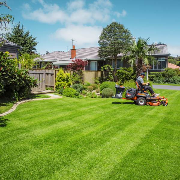 Professional gardener using ride-on lawn mower to maintain a neatly trimmed residential lawn in a suburban neighborhood